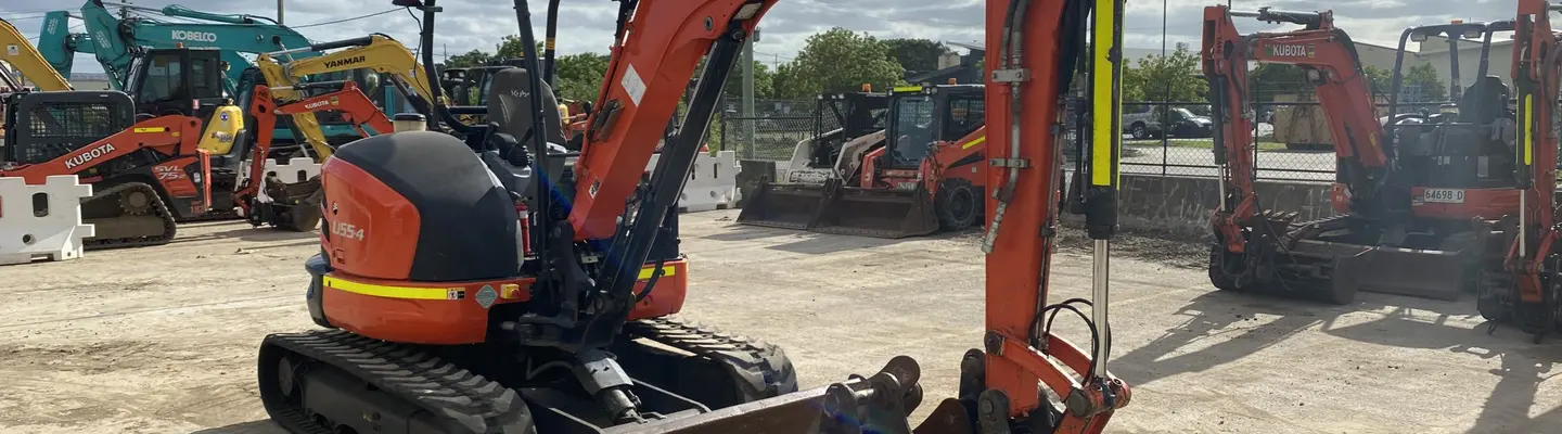 Lineup of used excavators on display at a construction yard, with safety signs and barriers marking the viewing area.