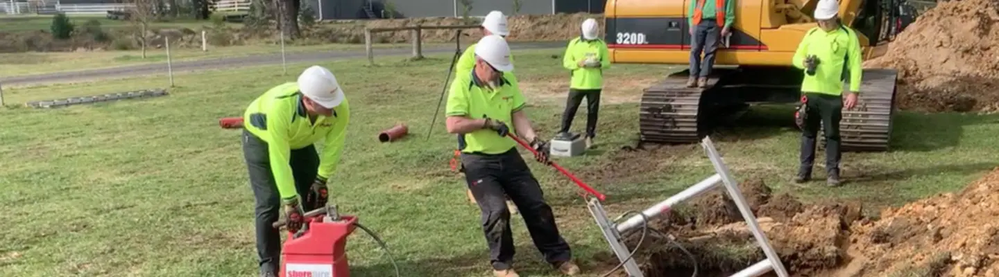 Construction workers digging a trench and placing metal supports in the ground, following proper safety procedures.