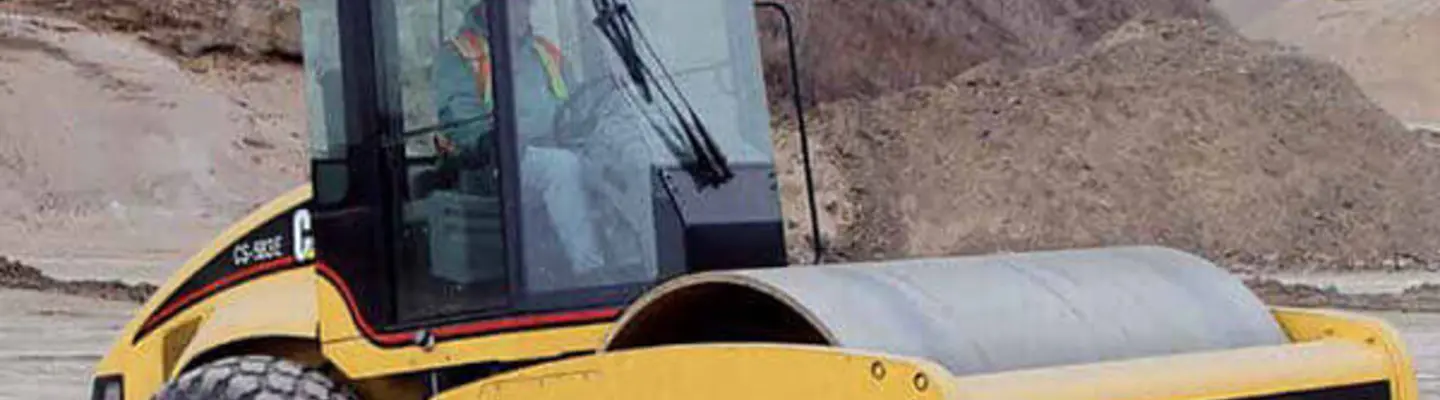 A Caterpillar compaction roller in use on a construction site, compacting soil to prepare a stable foundation for roadwork.