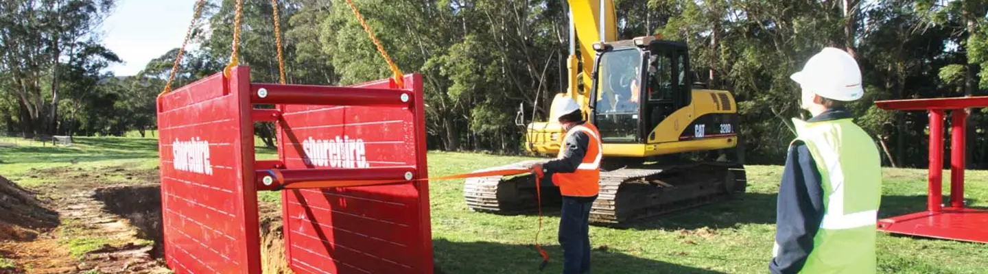 Workers lowering a protective box into an excavation site to ensure trench safety during construction work.