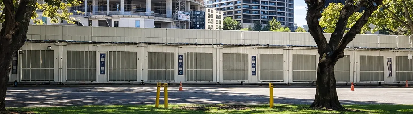 Pedestrian walking past buildings, trees, and a repurposed shipping container, highlighting urban design and green integration.