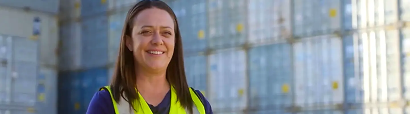 Company employee standing in front of a stack of shipping containers, used for storing and transporting construction safety barriers.