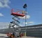 Side view of a scissor lift with red guardrails and gray base, operator using lift outdoors on level ground for rent.