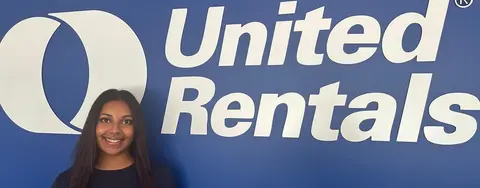 A woman standing in front of a blue wall with a big United Rentals logo on it.