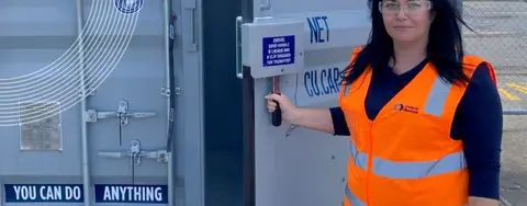 A woman in a hi-vis vest holding the door of a shipping container open.