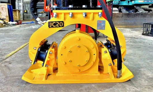 Plate compactor machine on a construction site near safety barriers, used for compacting soil and maintaining ground stability.