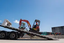 A man operating a tracked trailer vehicle on a construction site, transporting materials across rough terrain.