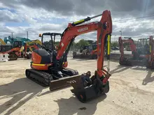 Lineup of used excavators on display at a construction yard, with safety signs and barriers marking the viewing area.