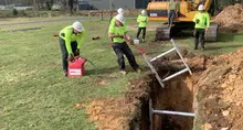 Construction workers digging a trench and placing metal supports in the ground, following proper safety procedures.