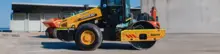 Standby compaction roller parked near construction barriers, ready for ground stabilization work on the site.