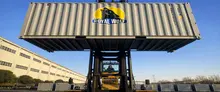 A 20ft Wolf-lock Shipping Container being lifted by a forklift, suspended above the ground in an industrial yard.