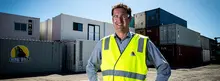 Manager standing in front of a stack of shipping containers at a work site, overseeing logistics and construction safety operations.