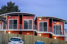 Two-story modular housing units made from shipping containers with exterior stairs and balconies at dusk.