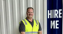 Man standing and smiling confidently in an outdoor setting, conveying positivity and professional presence.