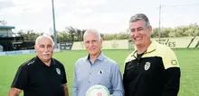 Three men smiling and holding a football on a grassy field, enjoying a friendly moment outdoors.